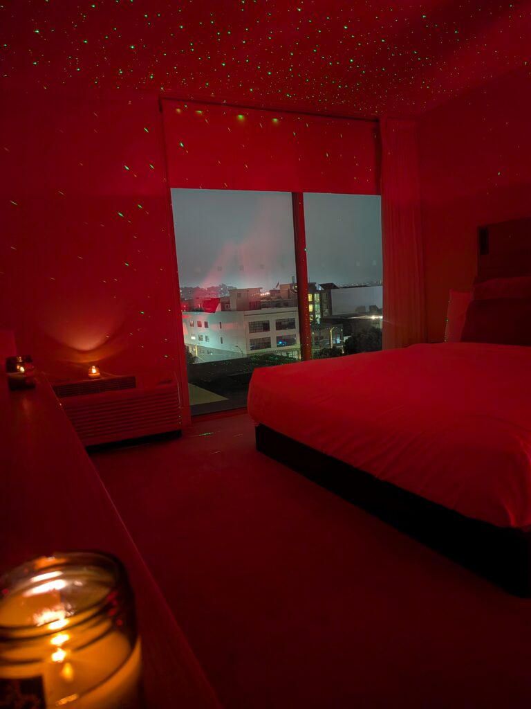 Moody red-lit production setting with a bed, candlelight, and projected star lighting